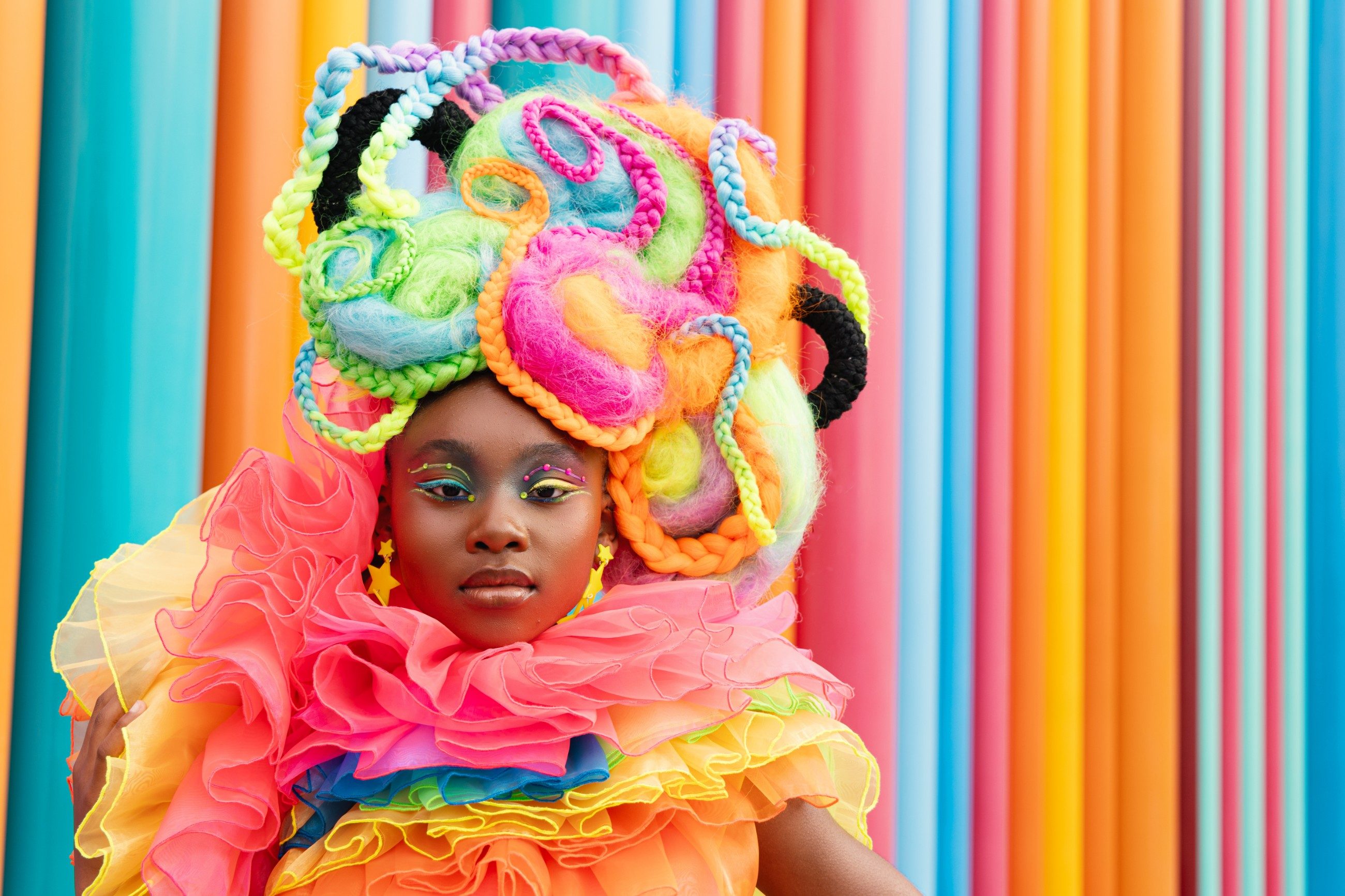 Girl in a neon braided wig and ruffles against a striped colour wall