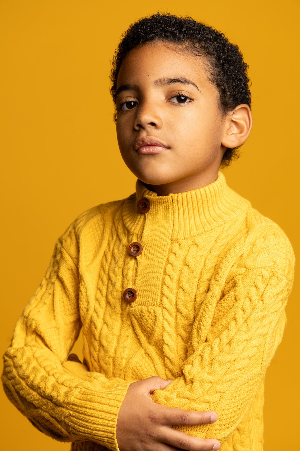 Boy in a yellow cable knit sweater, arms crossed