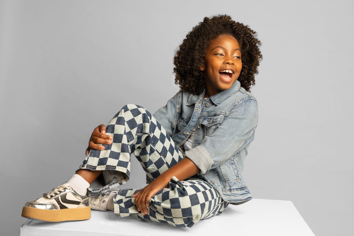 Girl in a denim jacket and checkered pants, seated and laughing