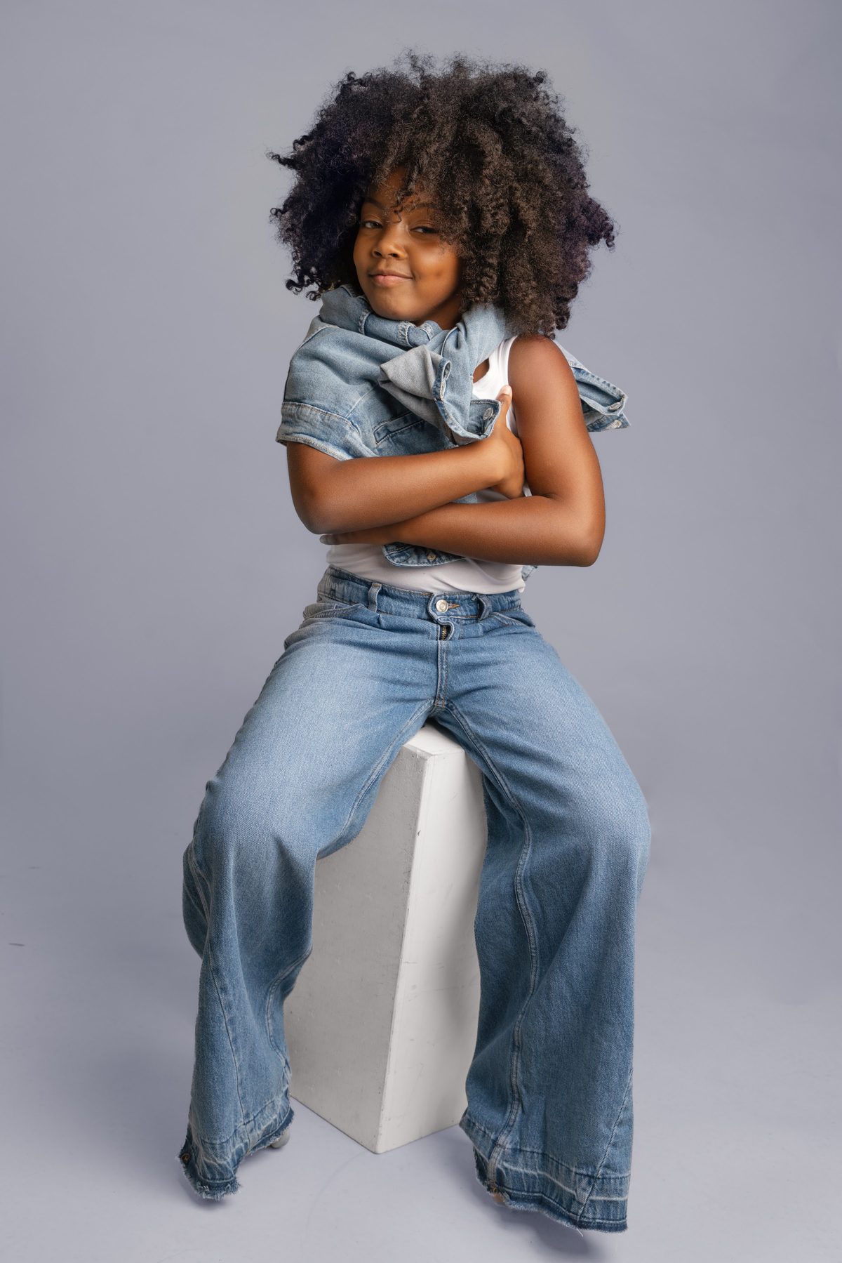 Girl in double denim with her arms crossed, seated on a white block
