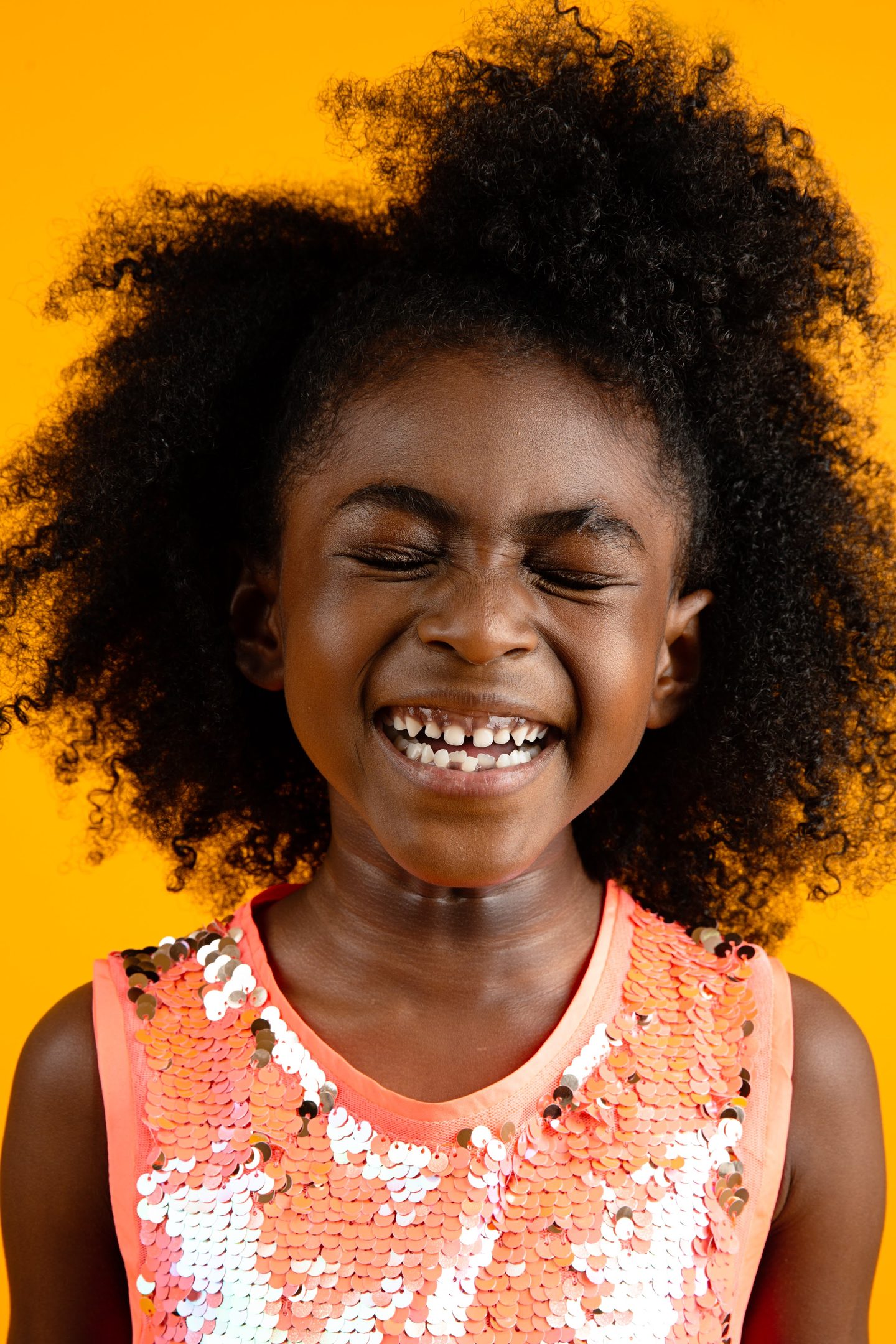 Girl laughing in a floral top against a yellow backdrop