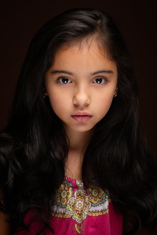 Girl in a pink embroidered top against a dark backdrop