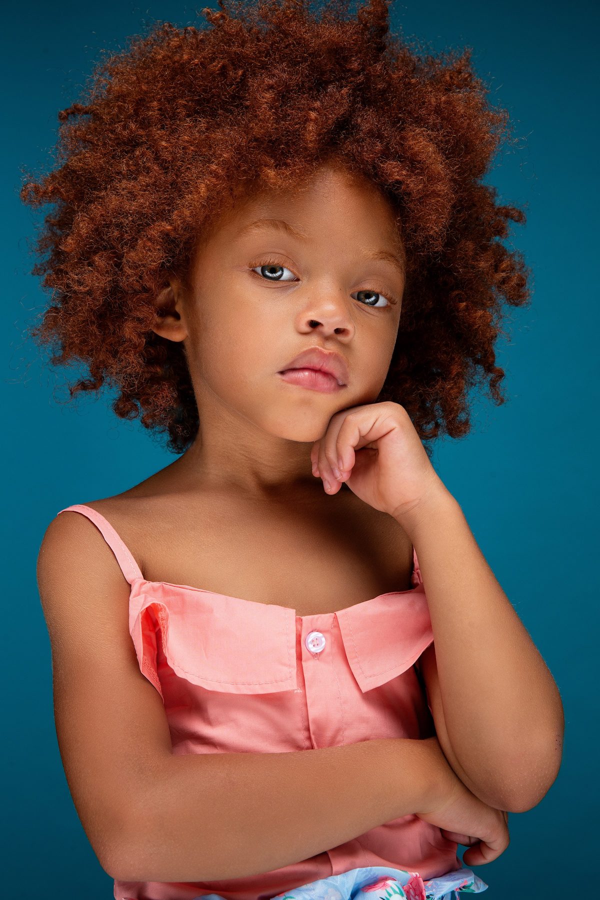 Girl with red curls in a pink top against a teal backdrop