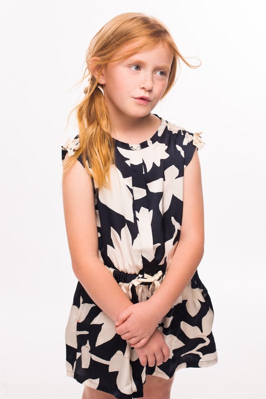 Red-haired girl in a floral dress standing with her hands clasped