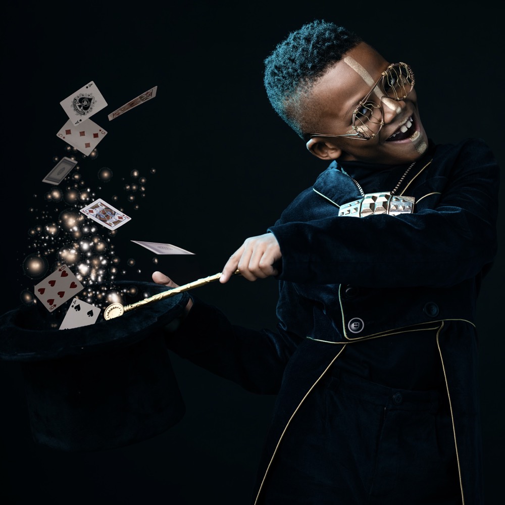 Child dressed as a magician conjuring cards from a top hat