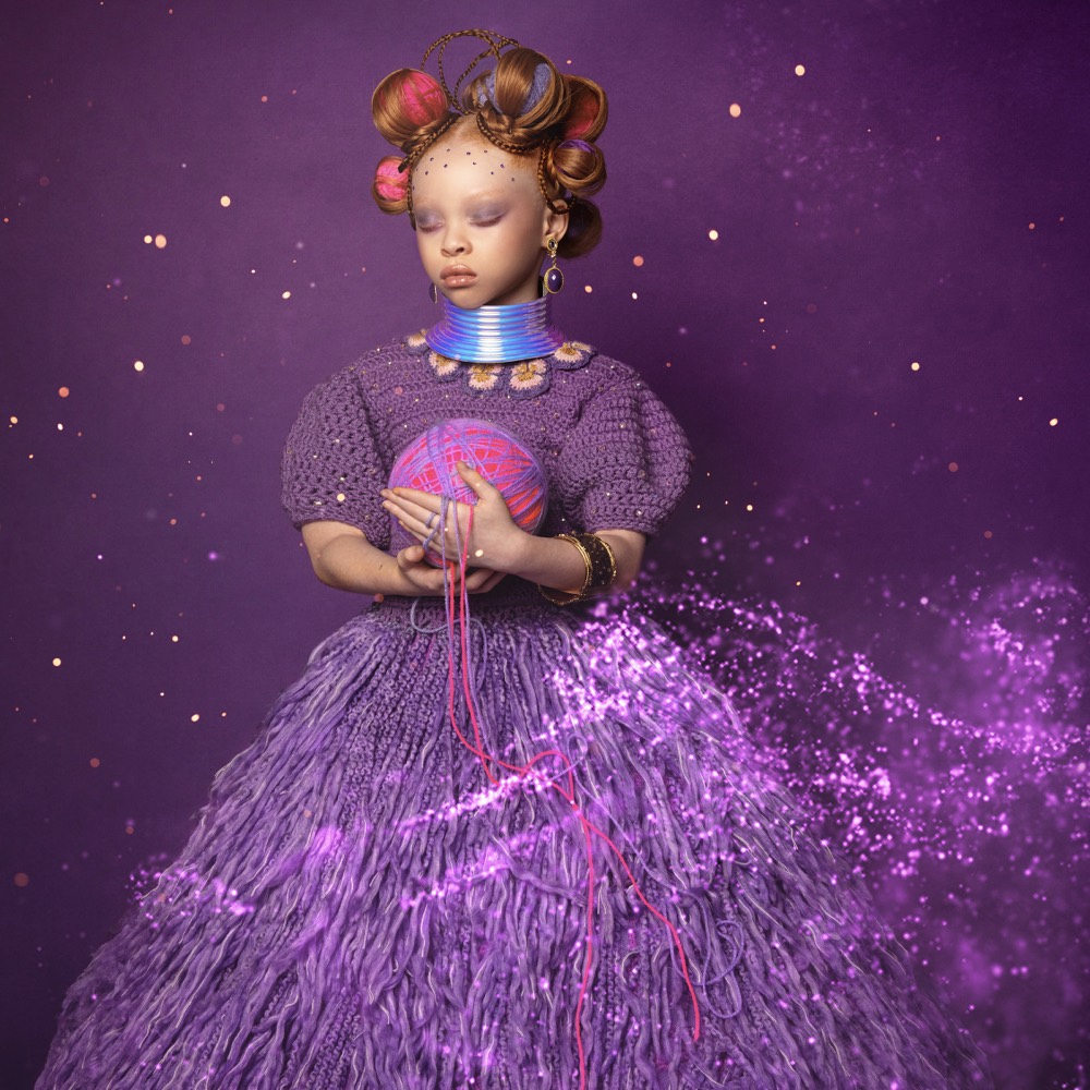 Child in a purple yarn gown holding a ball of yarn
