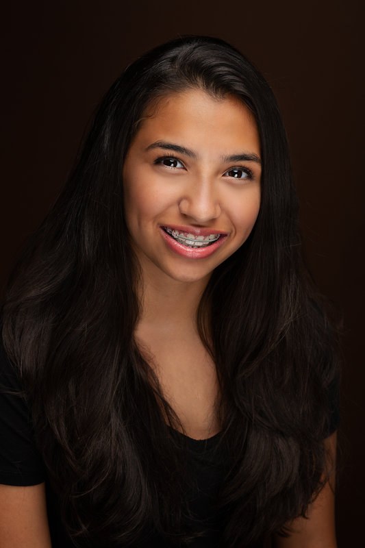 Teen girl smiling with braces against a dark backdrop