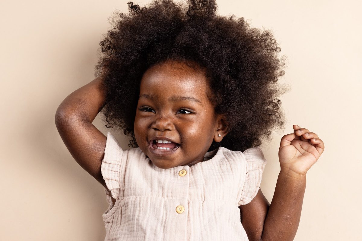 Toddler in white with curly puffs, laughing