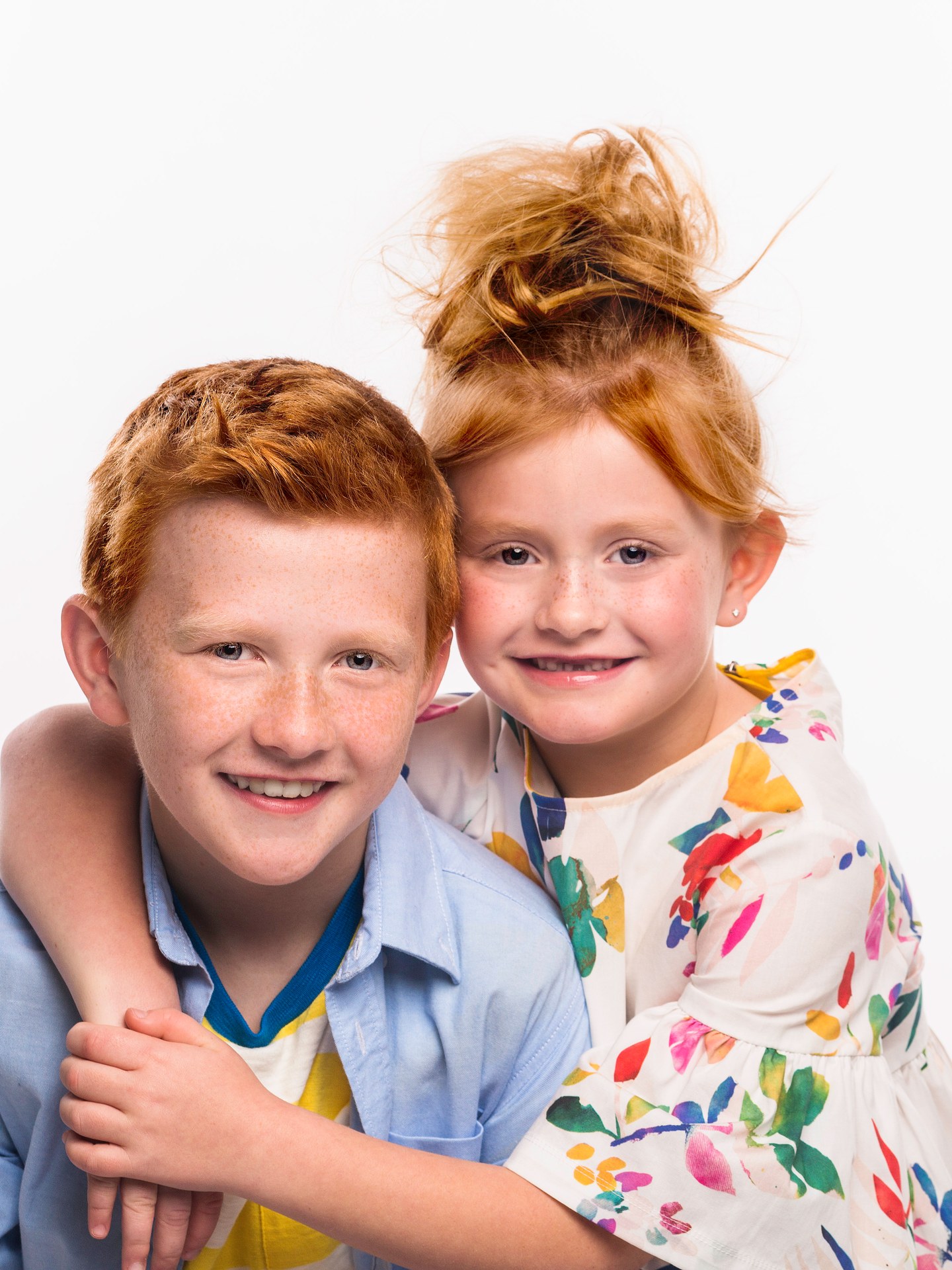 Two red-haired siblings hugging on a white backdrop