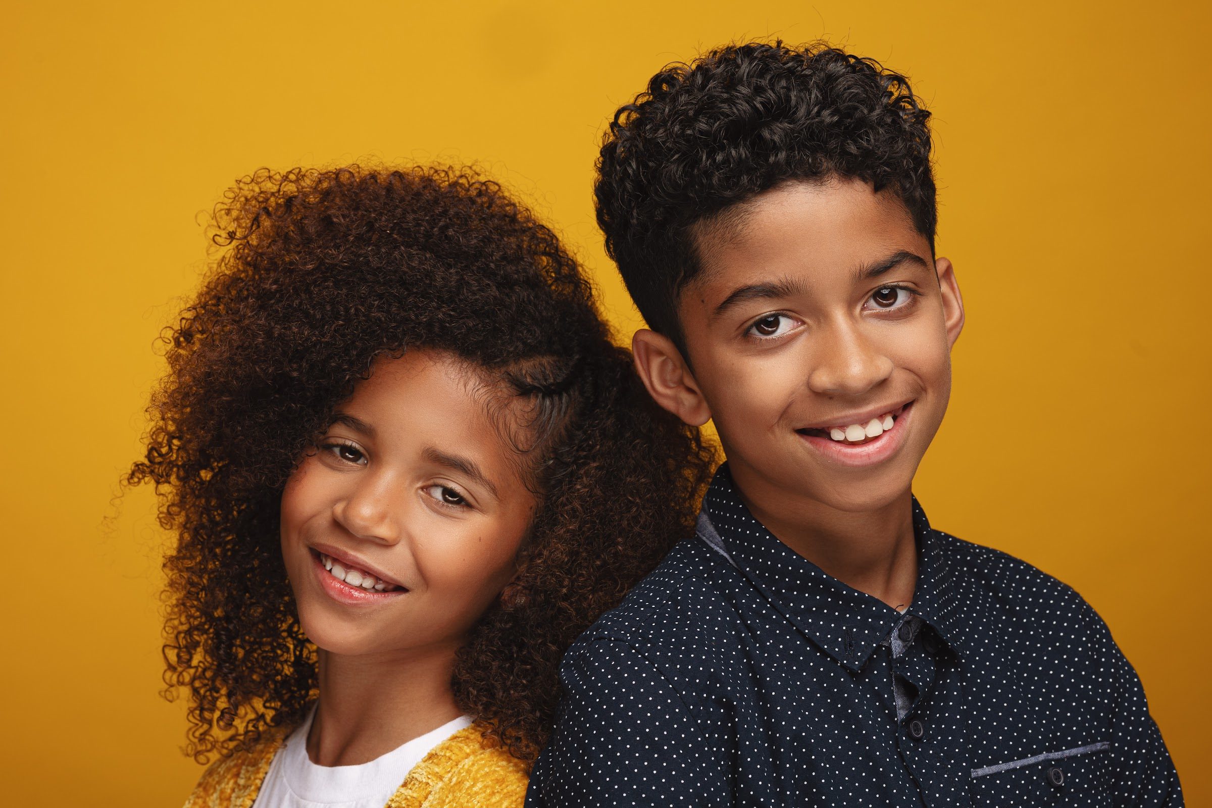 Two siblings side by side against a yellow backdrop