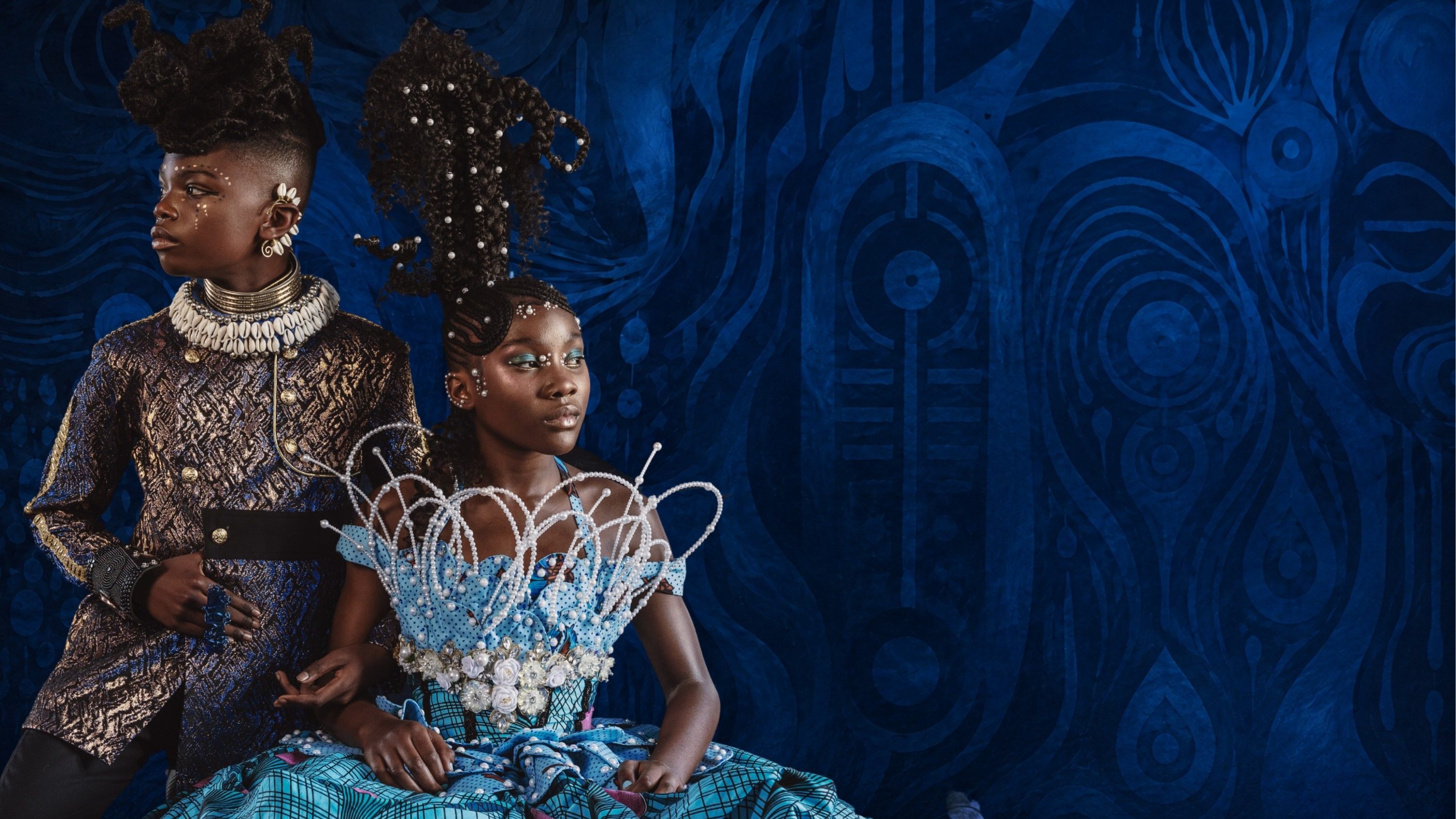 Two young models in blue royal styling against a painted indigo backdrop